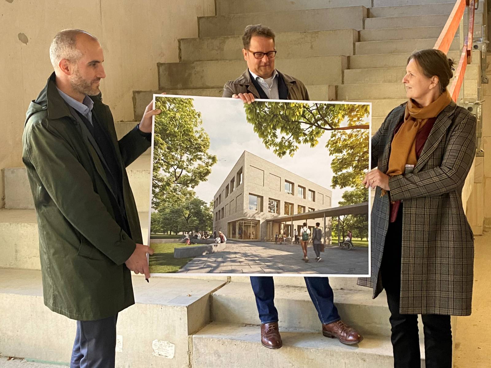 Drei Personen stehen in einem Rohbau und halten ein Bild, auf dem das fertige Gebäude zu sehen ist